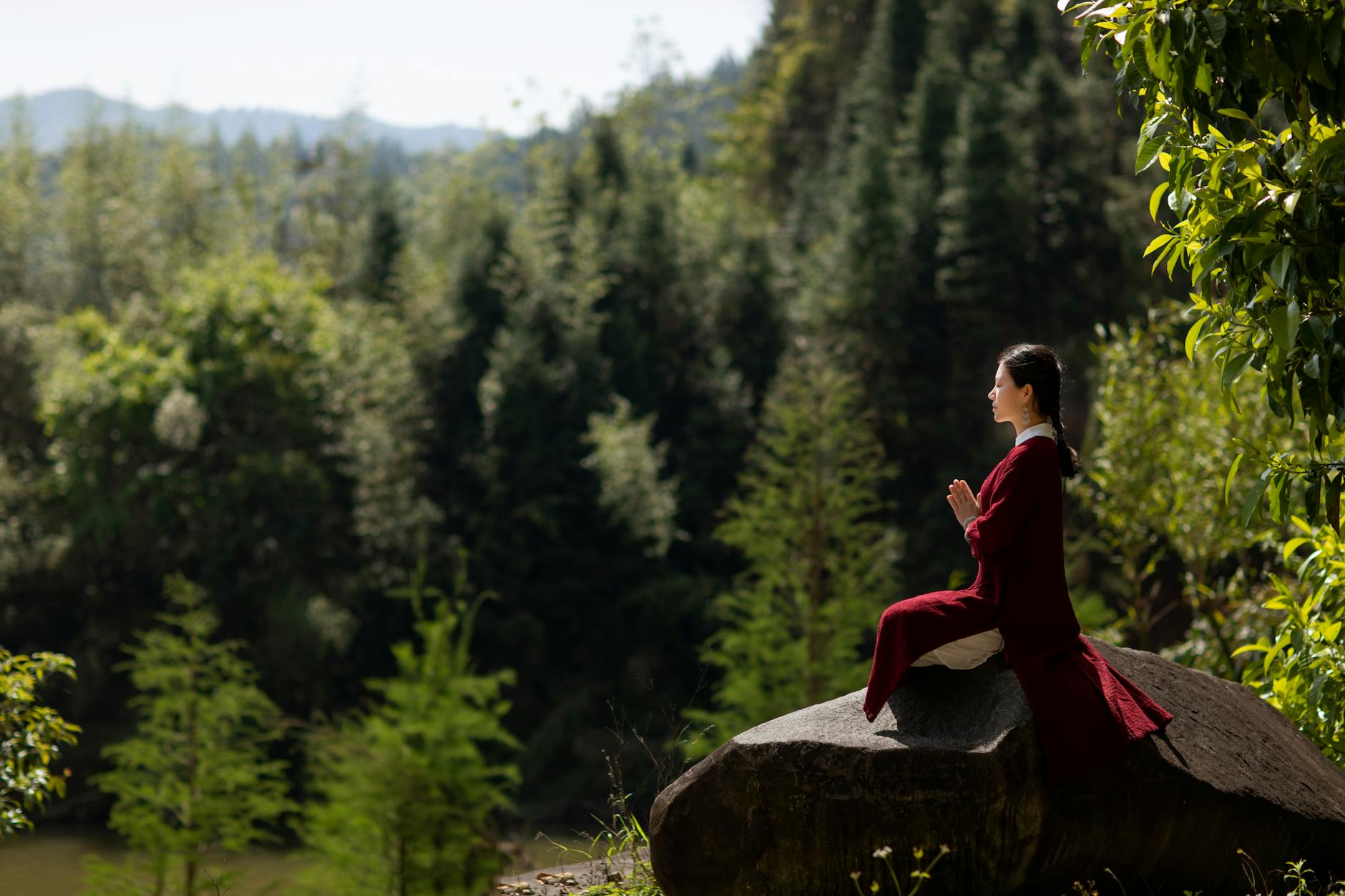 Azjatka w tradycyjnym stroju medytuje na skale w spokojnym lesie