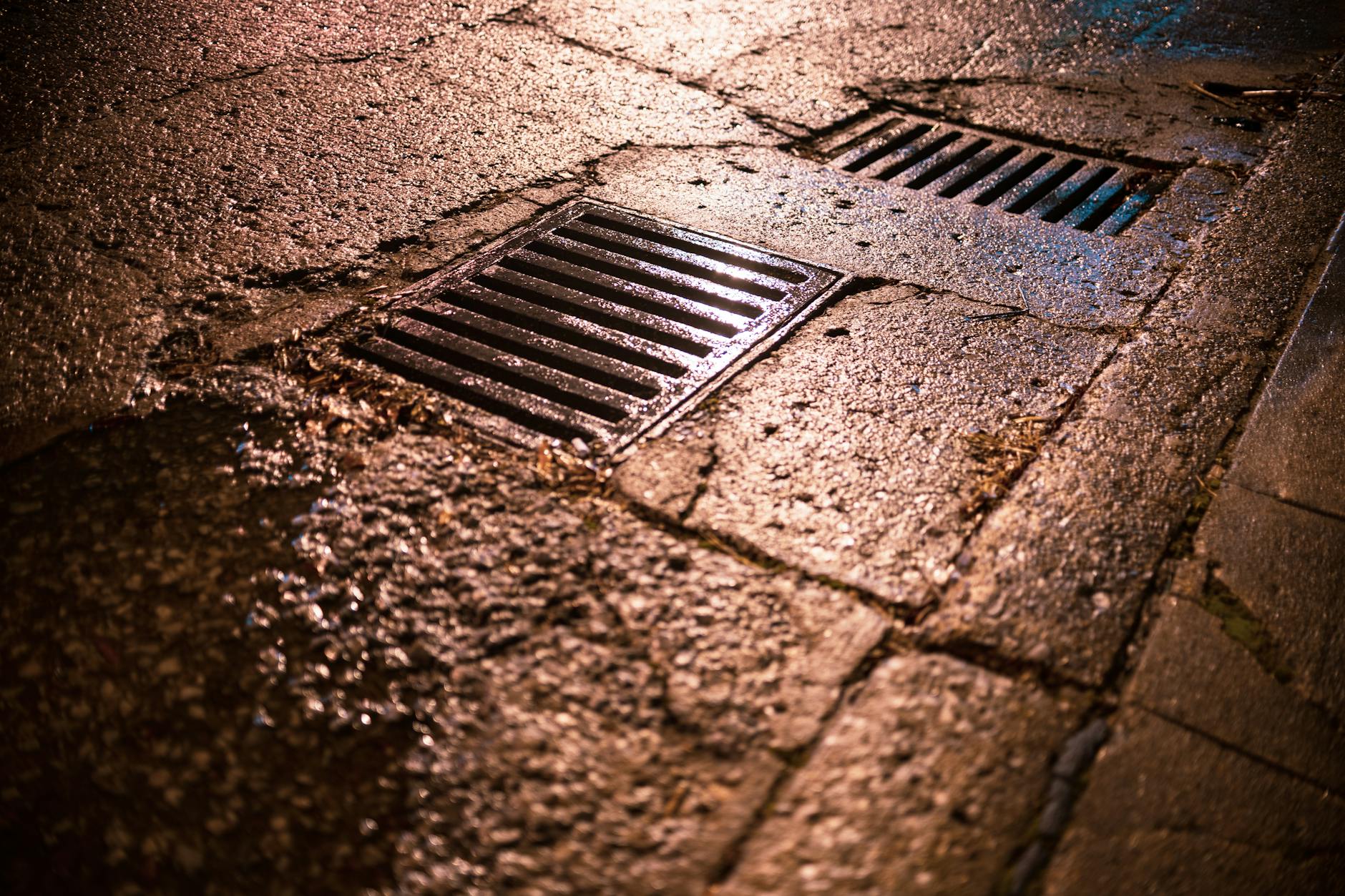 Nocne ujęcie mokrej jezdni z kratkami odwodniającymi