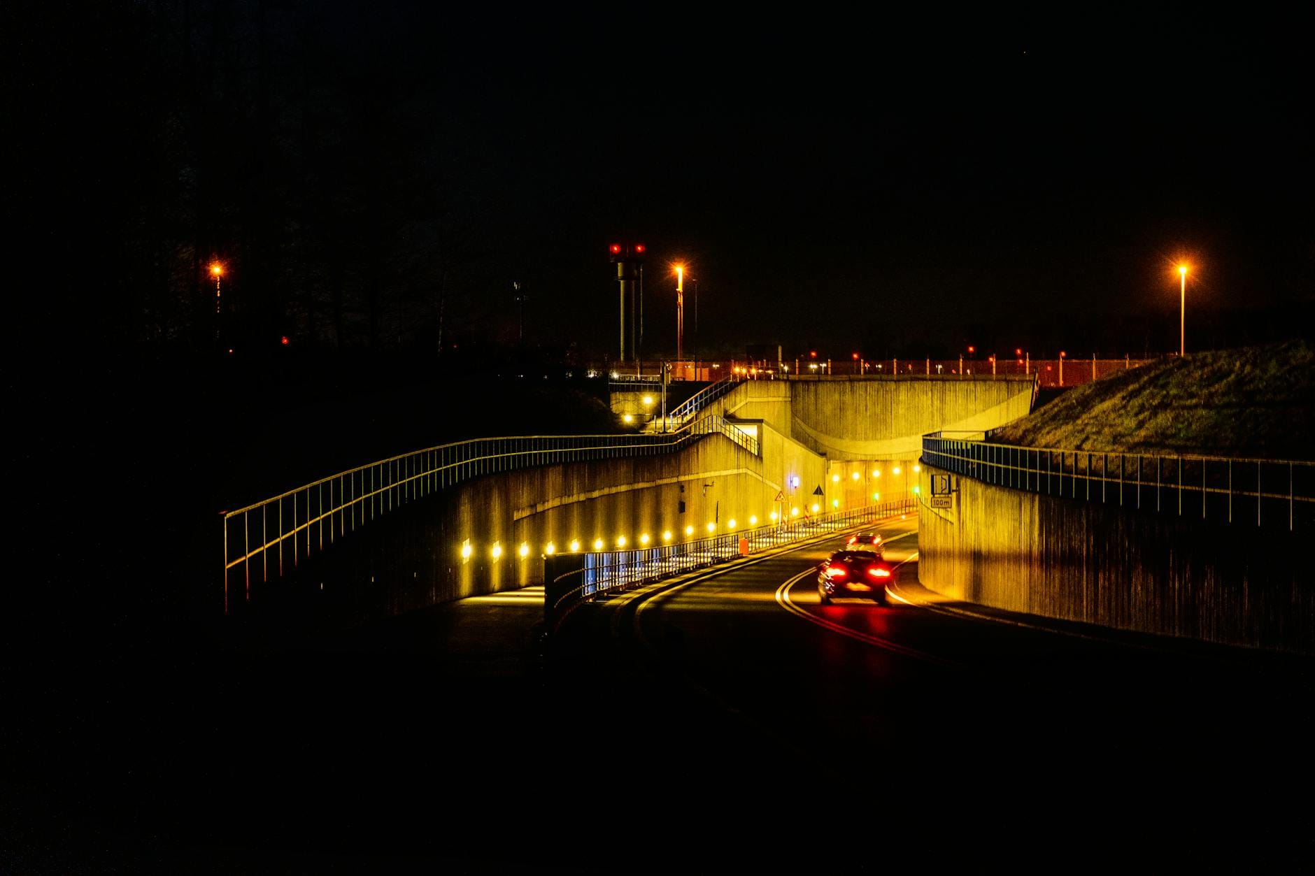 Samochód jedzie nocą oświetlonym tunelem z jasnymi lampami ulicznymi