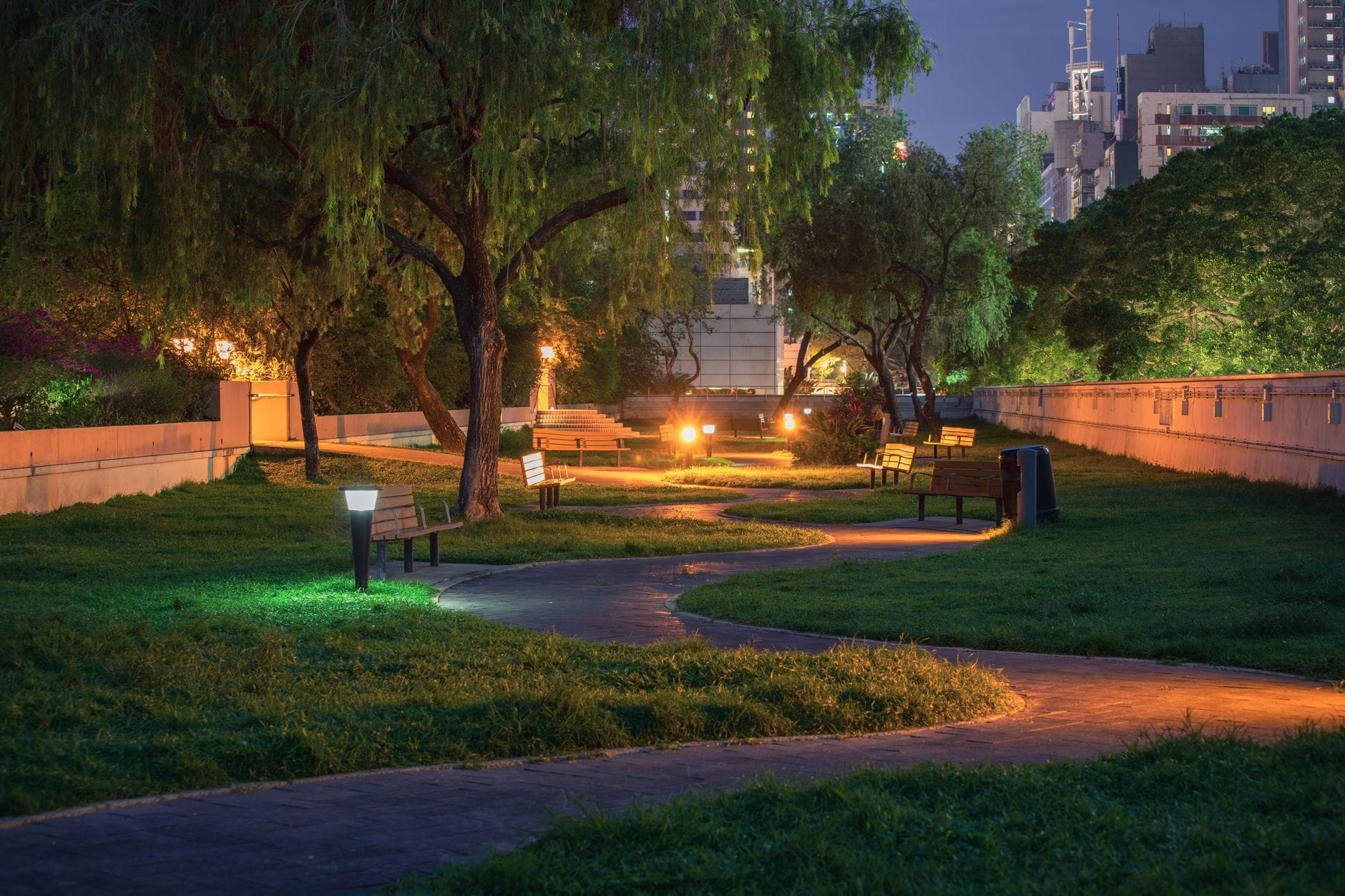 Nocny park miejski z oświetloną ścieżką i lampami przy ławkach