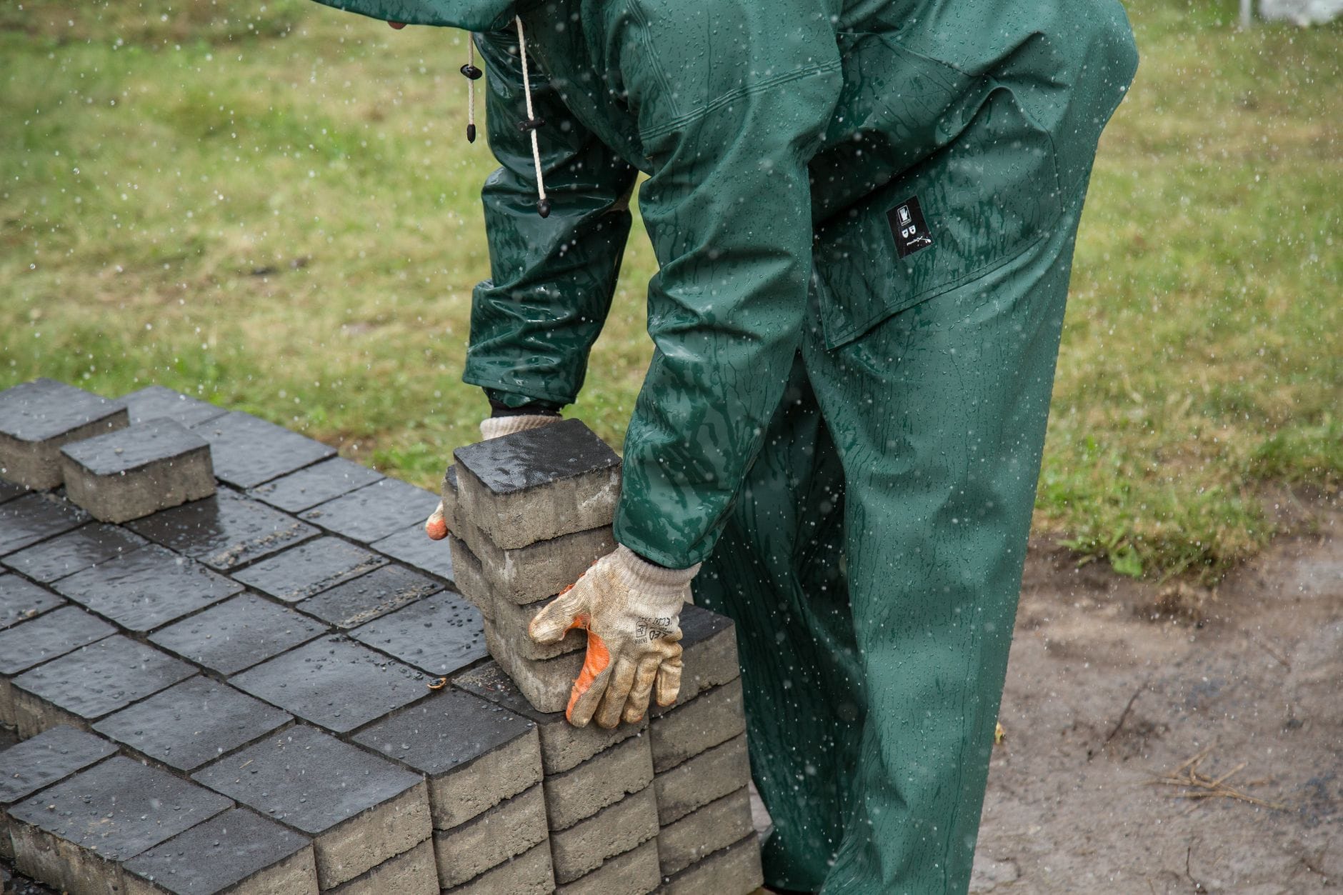 Pracownik układa kostkę brukową w deszczu na placu budowy
